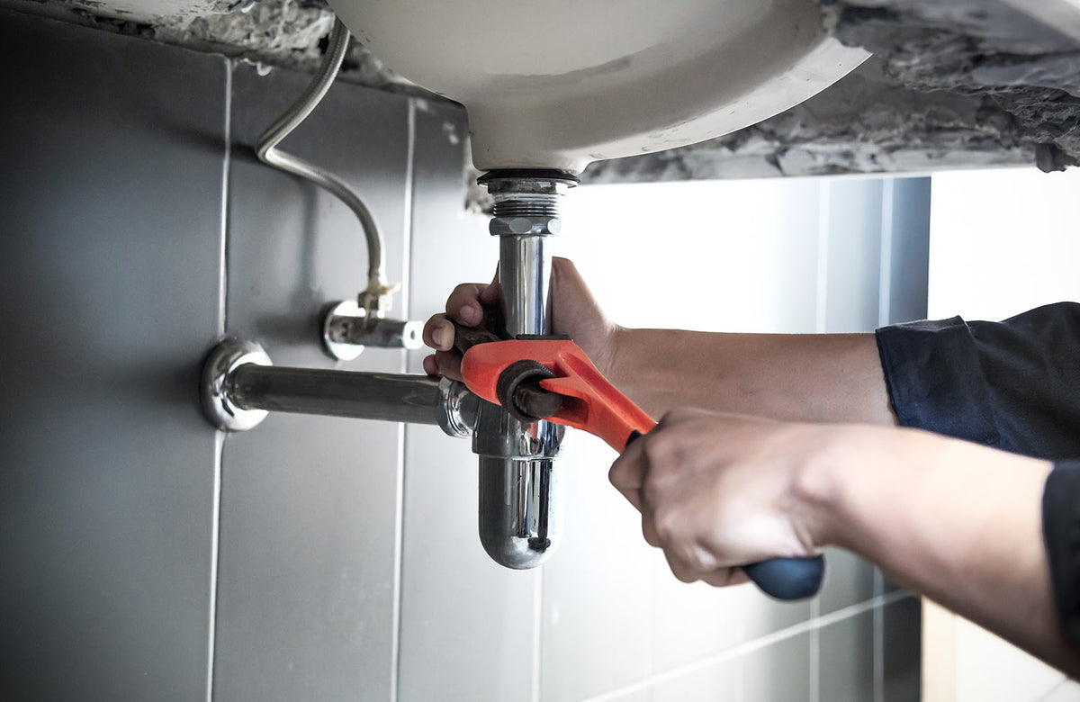 someone using a wrench to tighten pipes under a sink